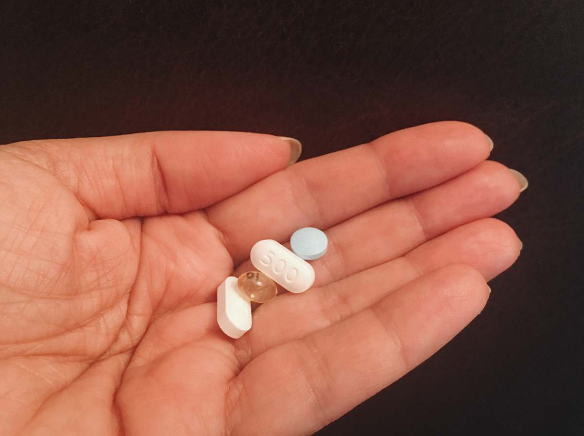 manicure person holding four assorted medicine tablets nail