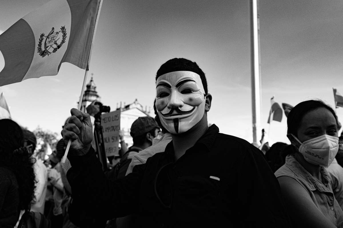 protester grayscale photo of man wearing mask and holding umbrella anarchy
