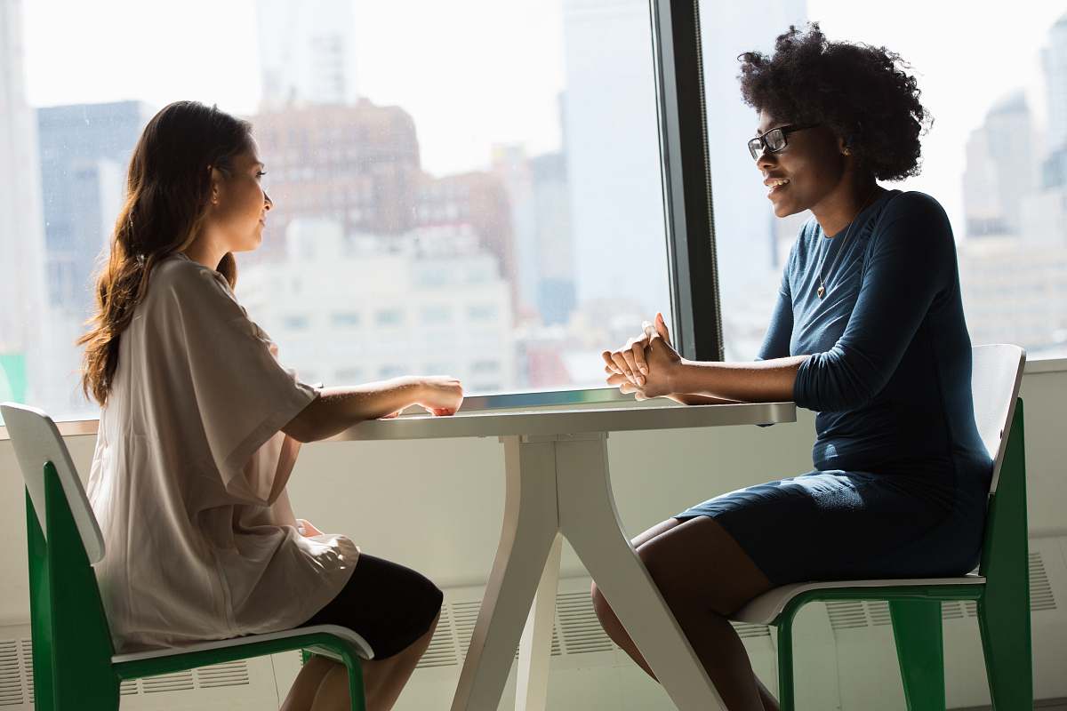 human two women sitting beside table and talking sitting