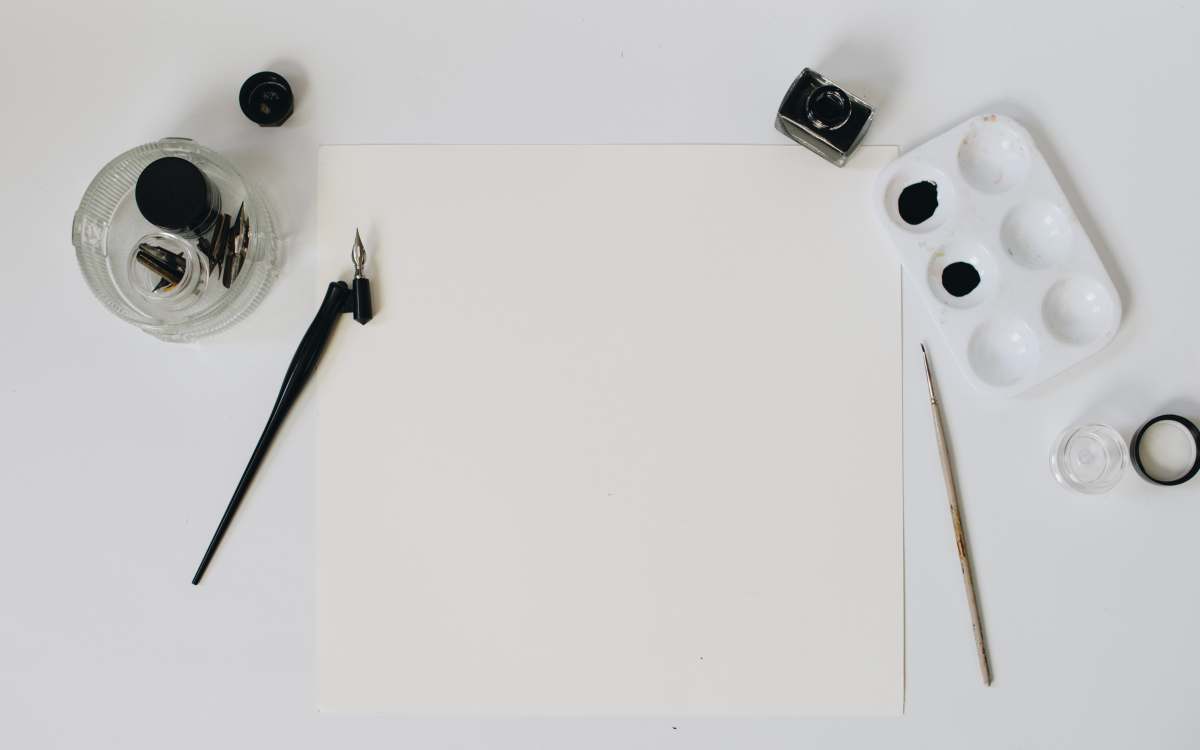writer black paint brush near paper, black ink, and glass jar holder