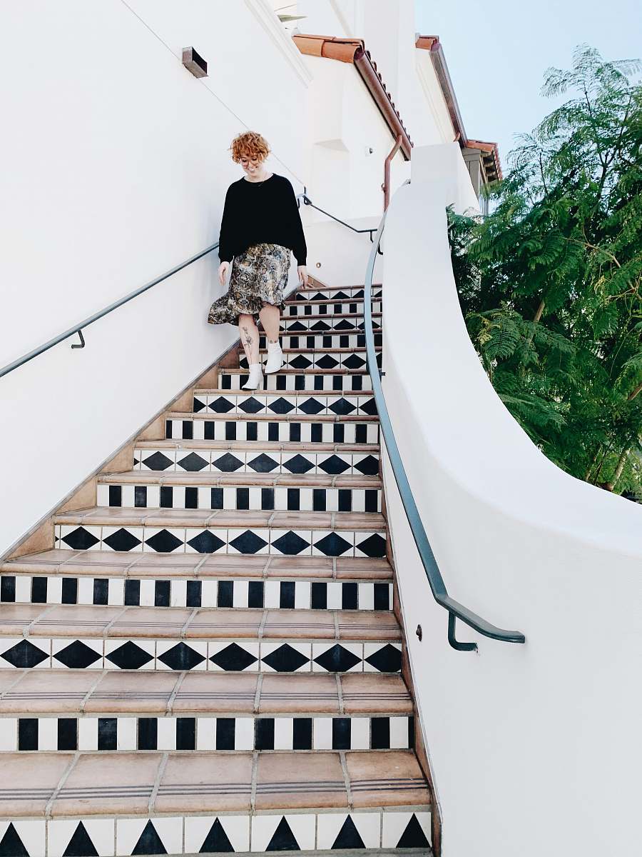 banister woman in white and pink floral dress walking down the stairs handrail