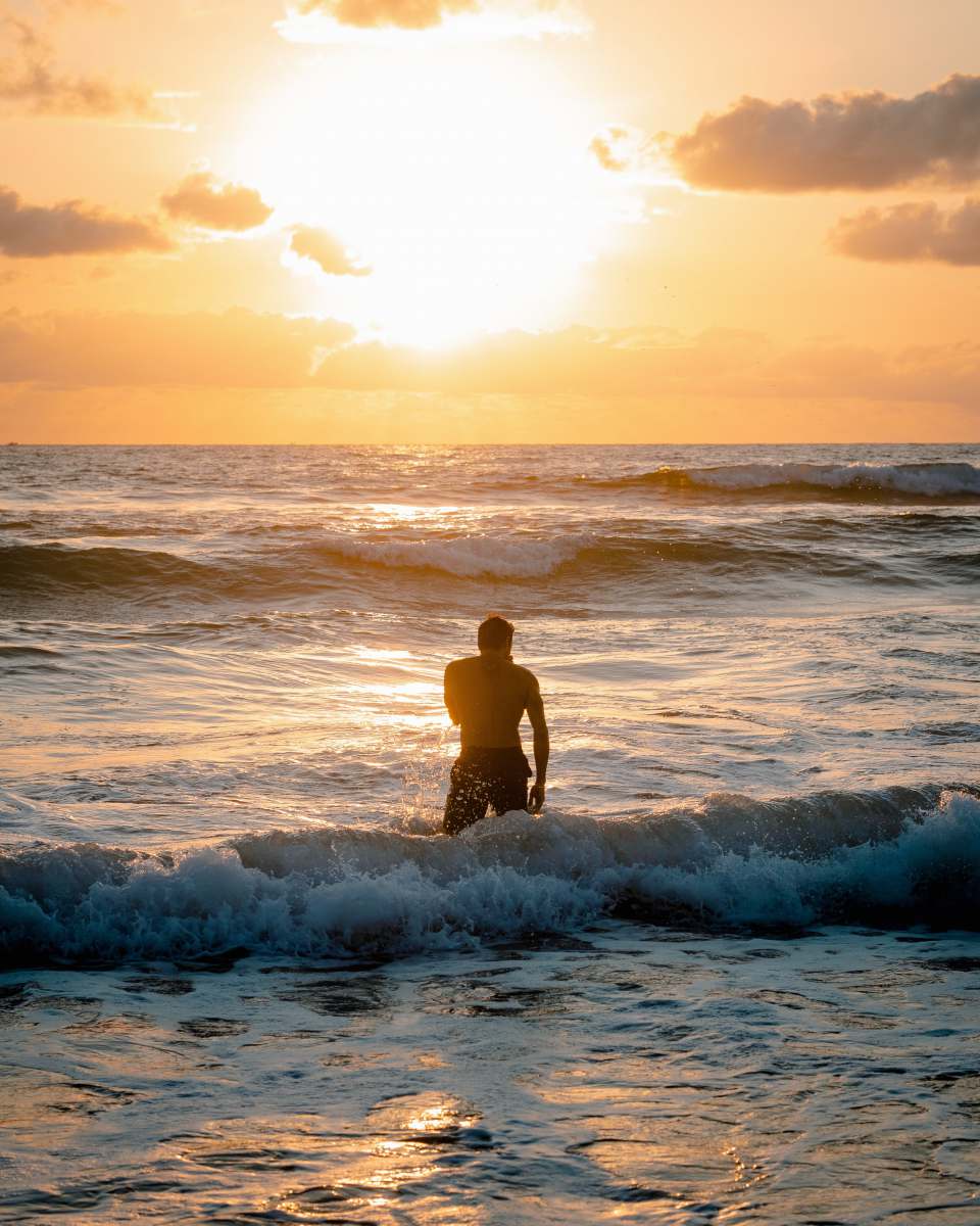 ocean man in black shorts standing on sea waves during sunset sunrise