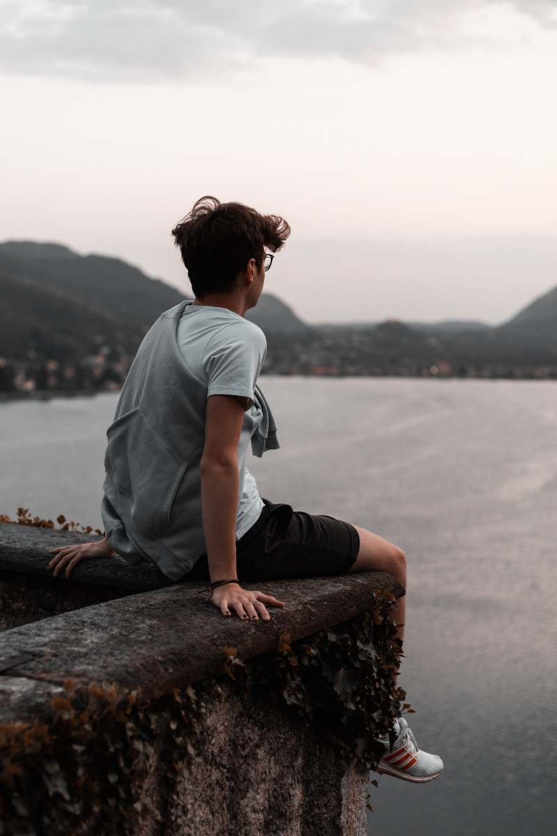  man in grey t-shirt and black pants sitting on brown rock near body of water 