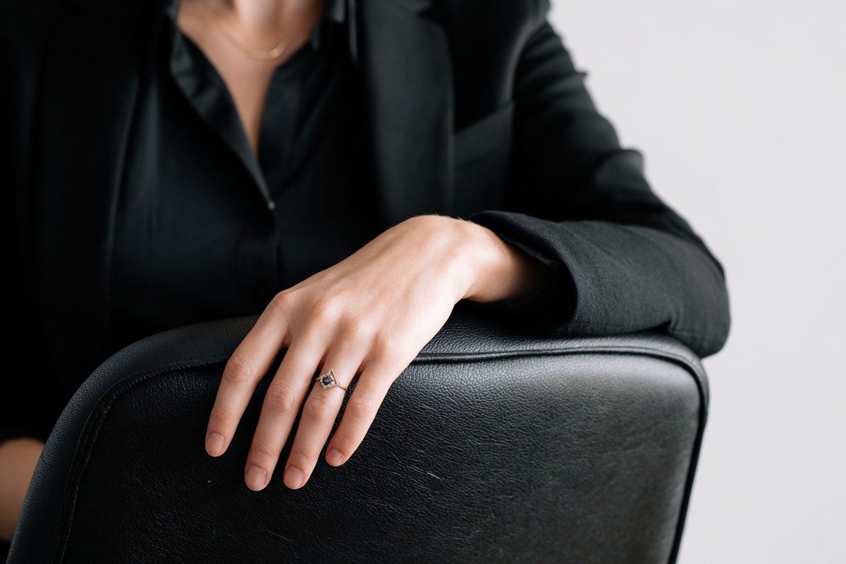 This close-up photograph captures a woman's hand adorned with a ring, delicately placed on the back of a chair. The image conveys a sense of elegance and contemplation, making it ideal for themes of femininity, style, and personal moments. Perfect for fashion blogs, lifestyle magazines, or advertisements focusing on jewelry and relationships.