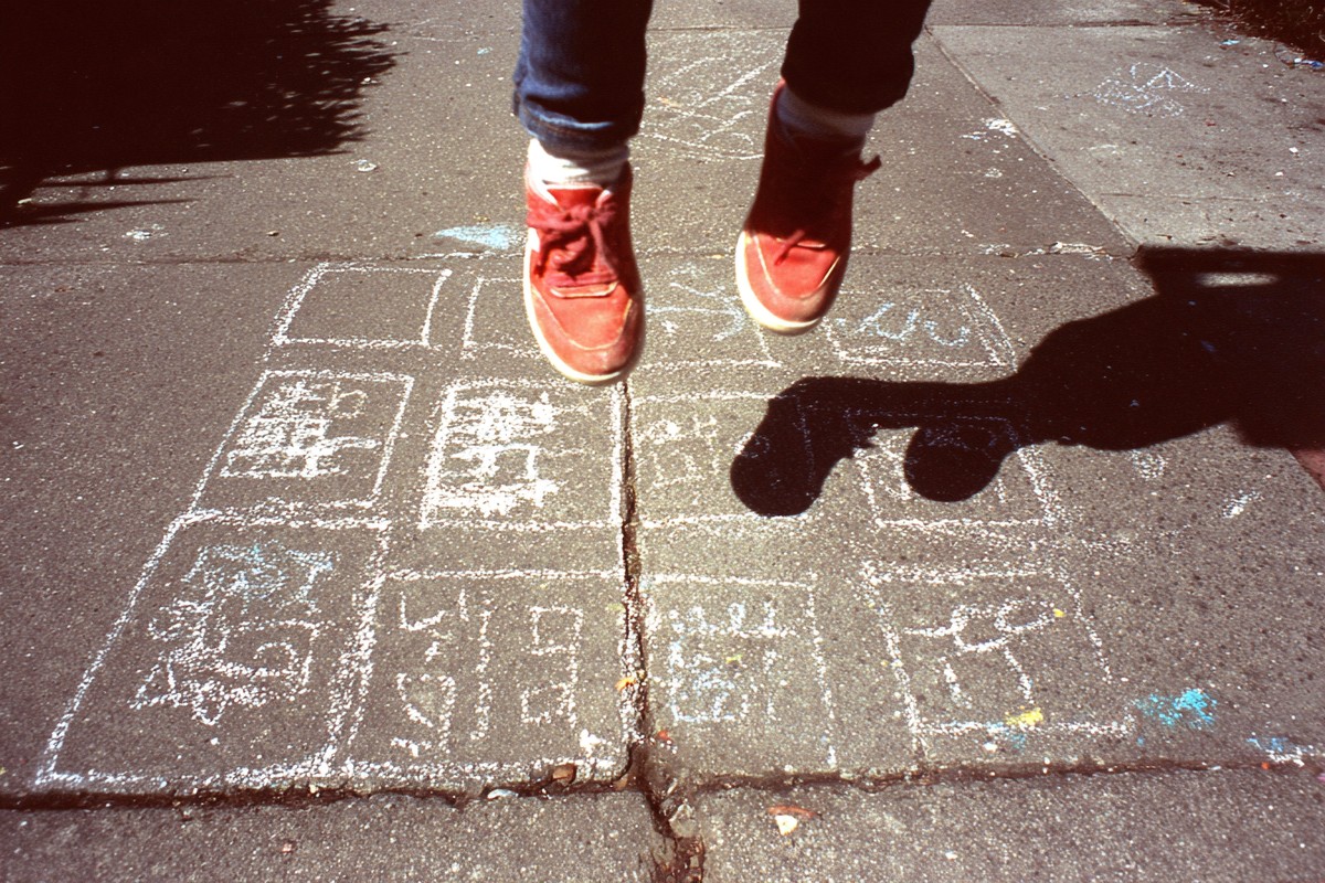 This image captures a child's feet playfully standing on a hopscotch drawn in colorful chalk on a sidewalk. The playful markings invite memories of carefree childhood days spent outdoors. Ideal for use in education, childhood development articles, or marketing campaigns targeting families that focus on outdoor activities and childhood play.