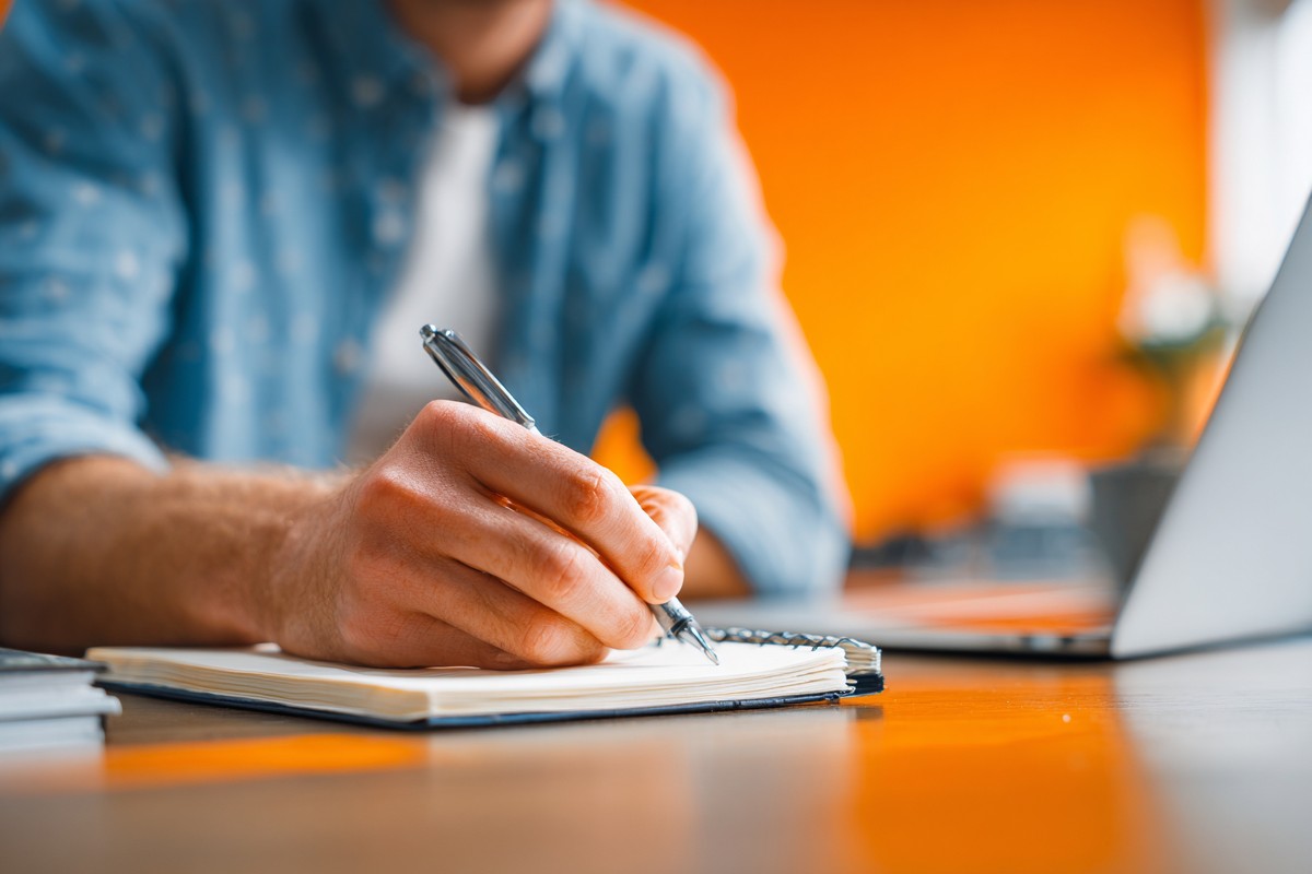 man blue shirt writing notebook with pen e940f0f1 64ac 4980