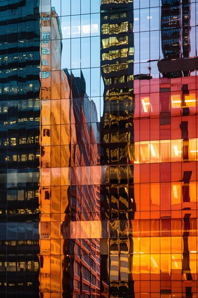 The reflection of a vibrant cityscape dances across the glass exterior of a high-rise business tower