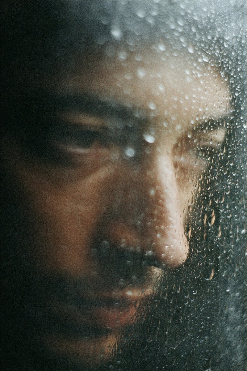 In a moment of introspection, a man gazes out the window, raindrops streaking down the glass like the thoughts clouding his mind. This image captures the essence of self-sabotage and inner conflict, making it ideal for topics related to mental health, personal growth, and overcoming challenges. It conveys a narrative of vulnerability and self-reflection.