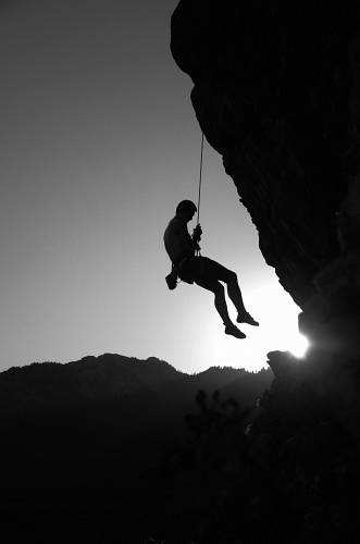 grey man hanging on cliff repel