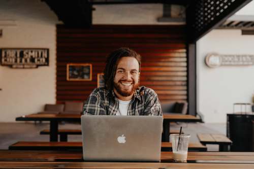 people man in black and white striped polo shirt sitting on chair in front of silver macbook laugh