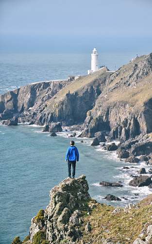 human man standing on rock with view of lighthouse and ocean person