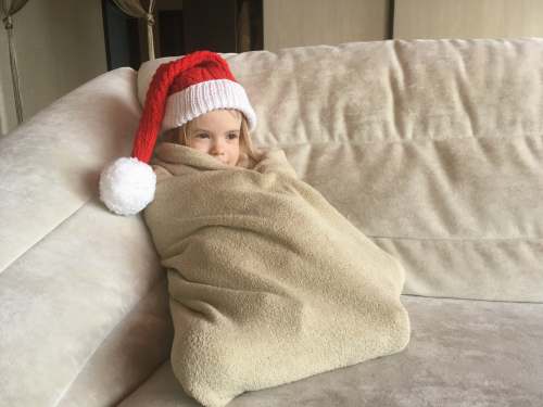 person baby in red and white santa hat lying on bed clothing