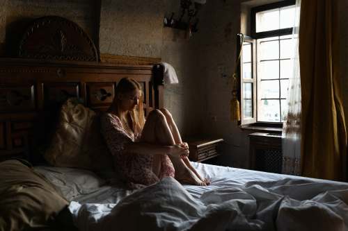 bed woman in white floral dress lying on bed shy