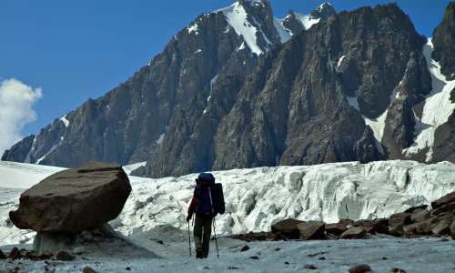 glacier man in black jacket and black pants with black backpack walking on snow covered ground during hiking