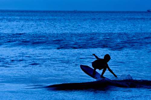 sea silhouette of boy on surfboard out at blue sea ocean