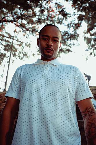 skin man in white and black star print polo shirt standing near green trees during daytime sleeve