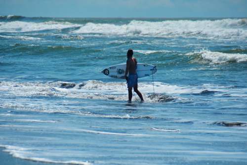 surfing man in black shorts holding white surfboard walking on beach during daytime lifestyle