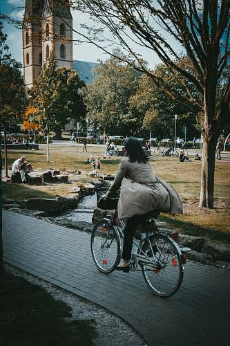 wheel woman in gray jacket riding bicycle on gray concrete road during daytime vehicle
