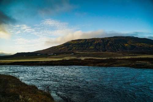 scenery green and brown mountain beside body of water under blue sky during daytime iceland