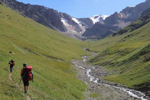 mountain person in red jacket and black pants walking on green grass field during daytime kok-art ridge