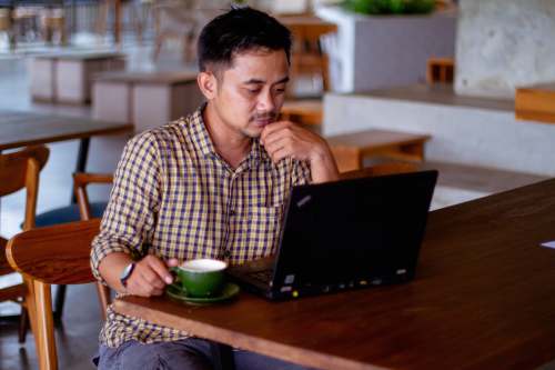 person man in black and white plaid dress shirt sitting in front of black laptop computer human