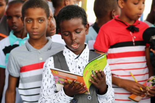 child man in red and white polo shirt holding yellow book boy
