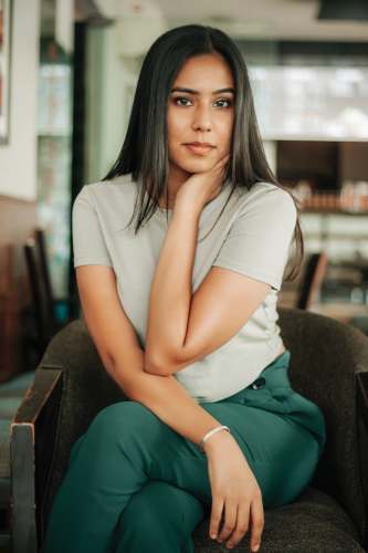 female woman in white t-shirt and green pants sitting on brown sofa apparel