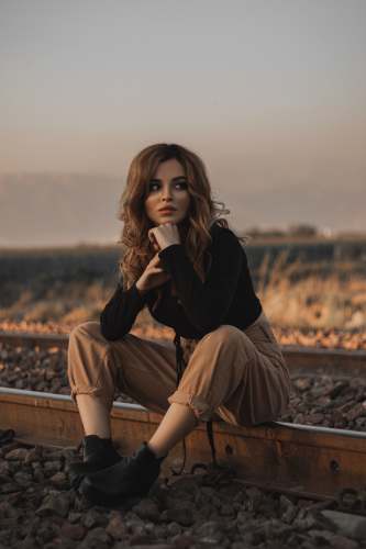 clothing woman in black long sleeve shirt and brown pants sitting on brown wooden bench during daytime person