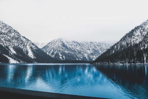 plansee landscape photo of clear blue body of water near mountains covered with snow 