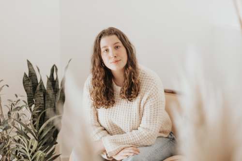 usa woman in white knit sweater and gray denim jeans sitting on white bed or
