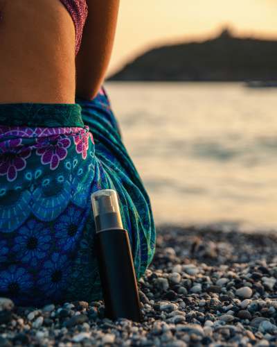  black bottle leaning on woman sitting on rocky shore during day 