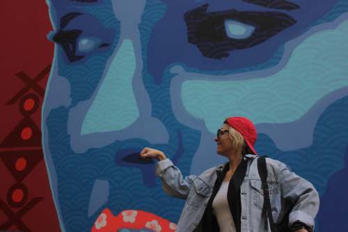  woman in gray denim jacket and red knit cap standing beside blue and white wall 