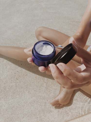 wellness person holding blue round plastic container face moisturiser