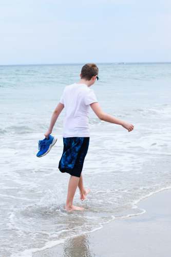  boy in white t-shirt and blue shorts running on beach during daytime 